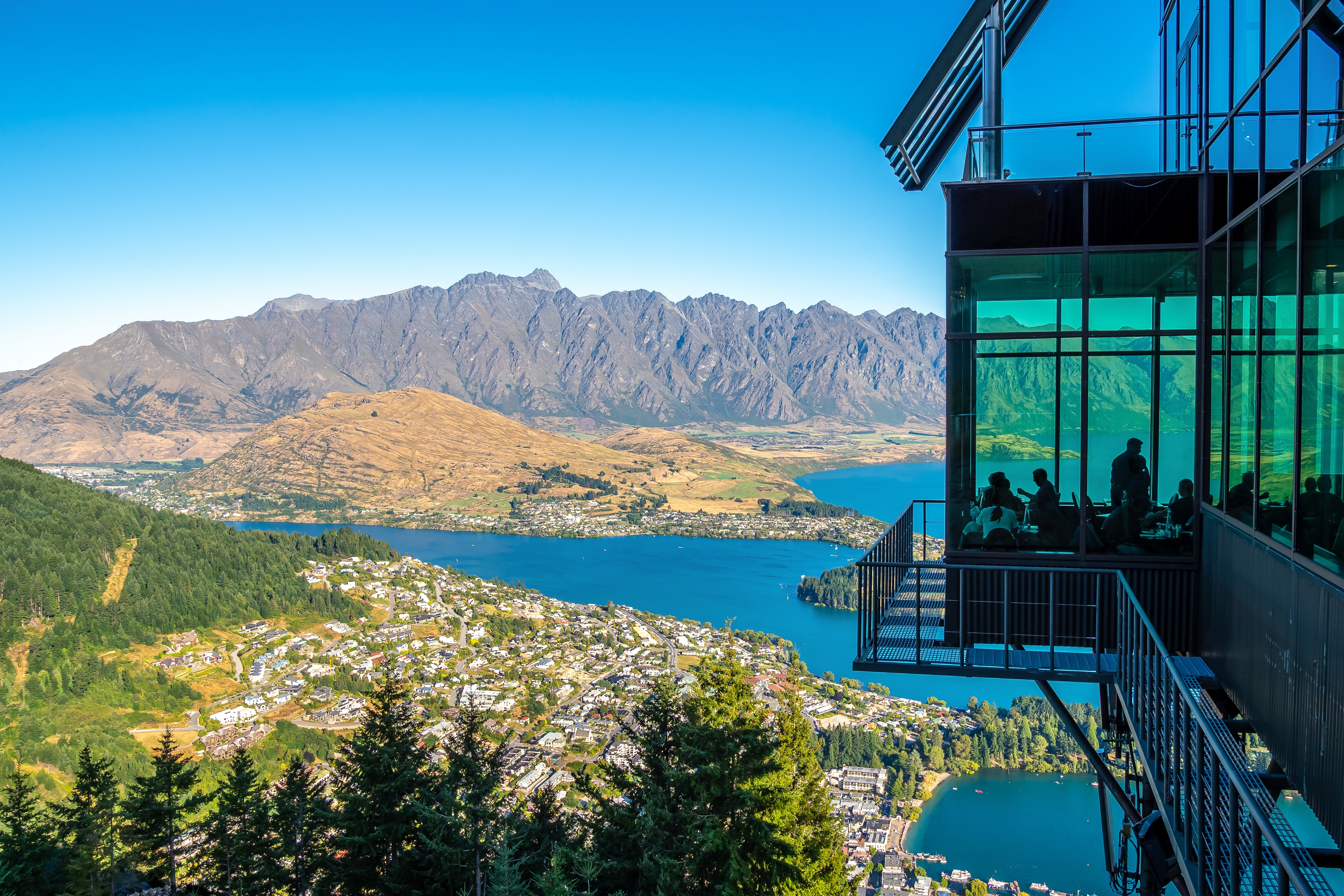 Scenic presumption of Queenstown, New Zealand with mountains, lake, and a glass-sided edifice overlooking the landscape