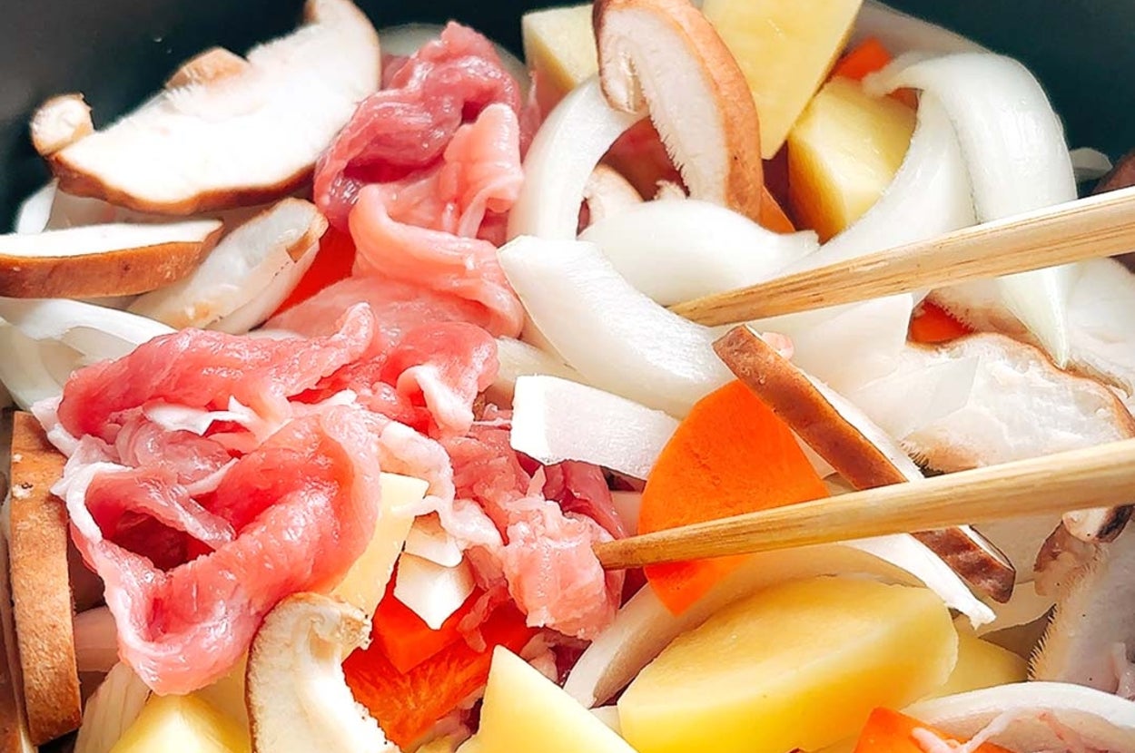 鍋の中に野菜やきのこと一緒に生の薄切り肉が入っている様子。箸も見える。