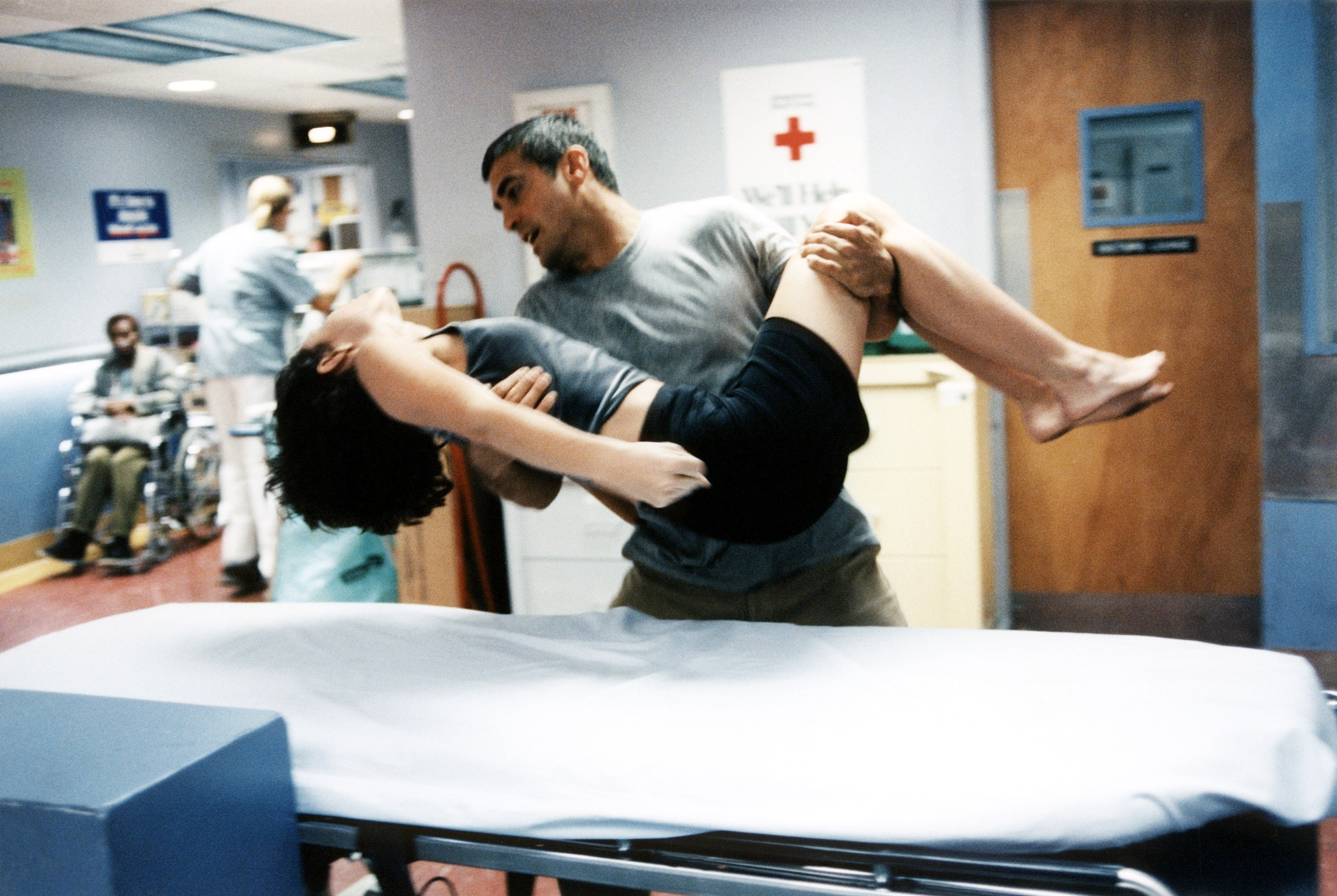 A person is being urgently carried through a hospital corridor, suggesting a dramatic scene possibly from a medical TV show or movie