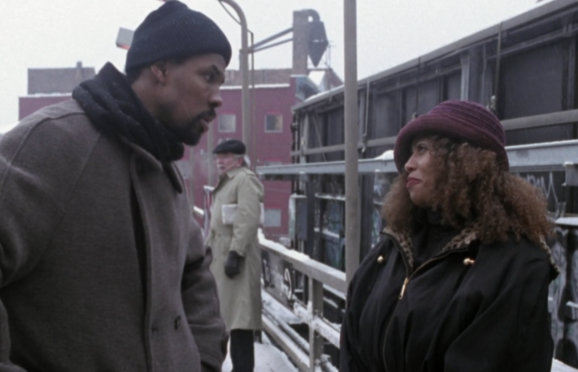 Two people in winter clothing have a conversation on a snowy train platform