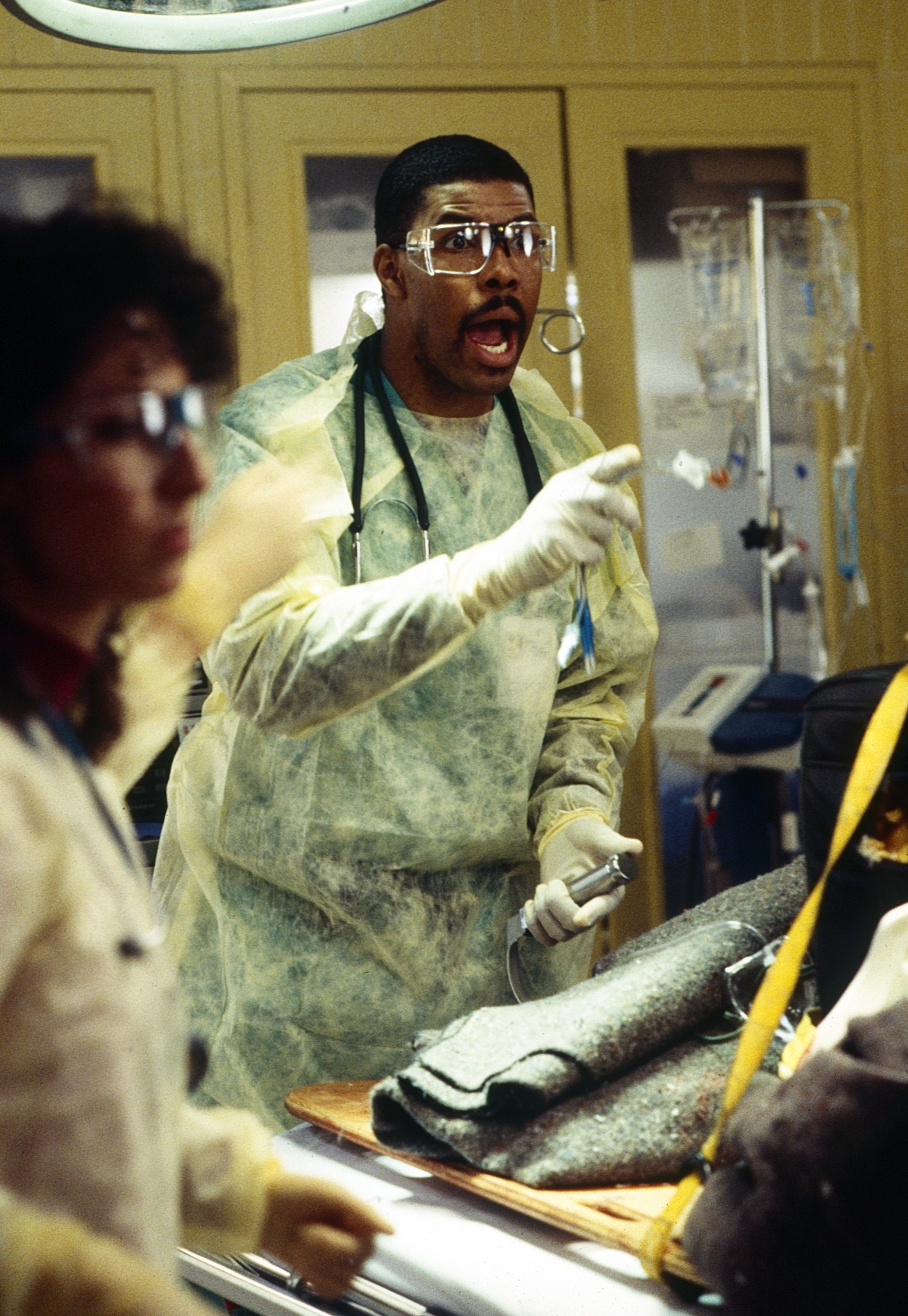 A medical professional in protective gear passionately speaks in a hospital setting, possibly from a scene in a TV drama or film