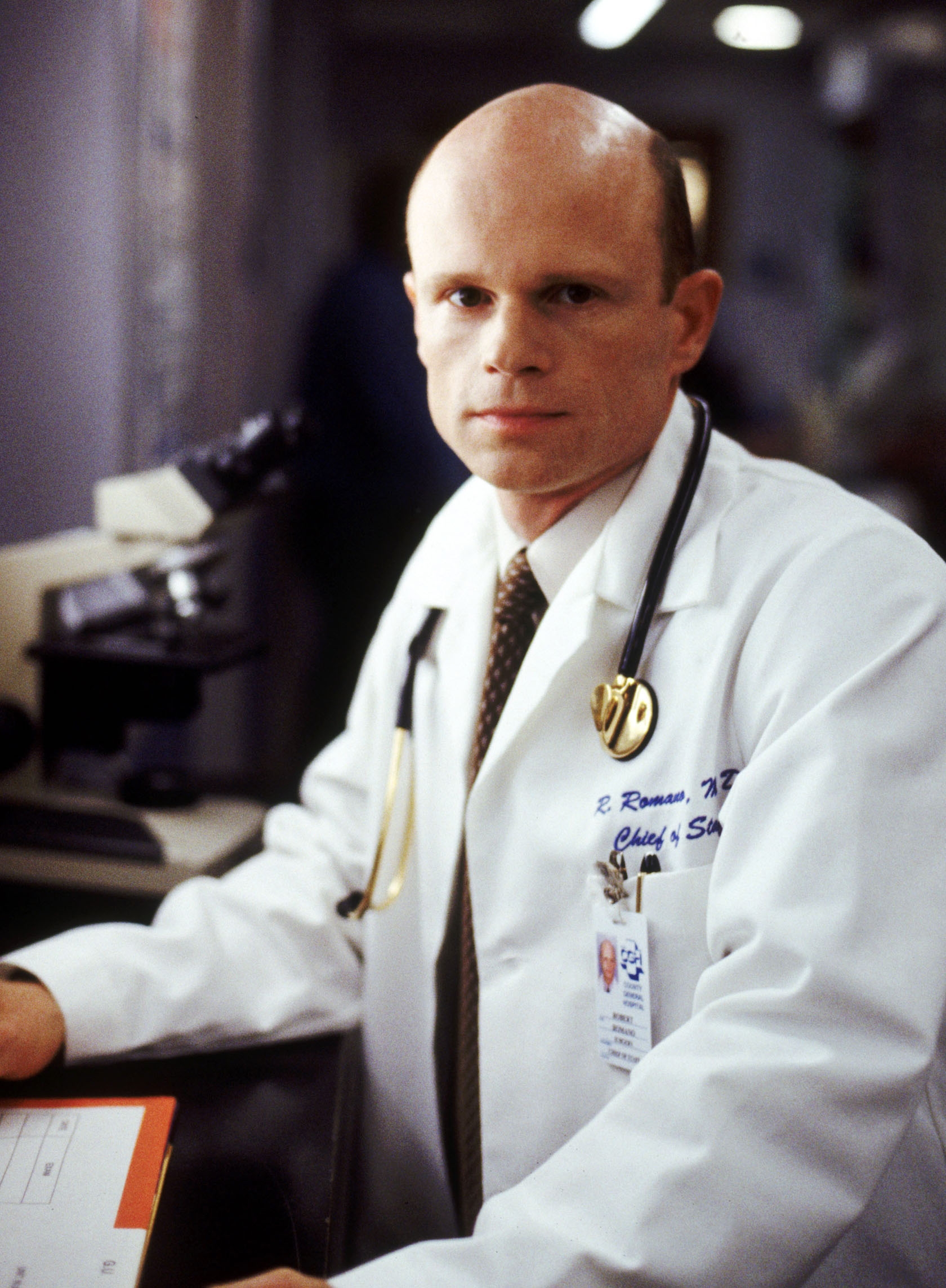 A doctor in a white coat with a stethoscope, standing in a medical setting near a microscope, looks focused