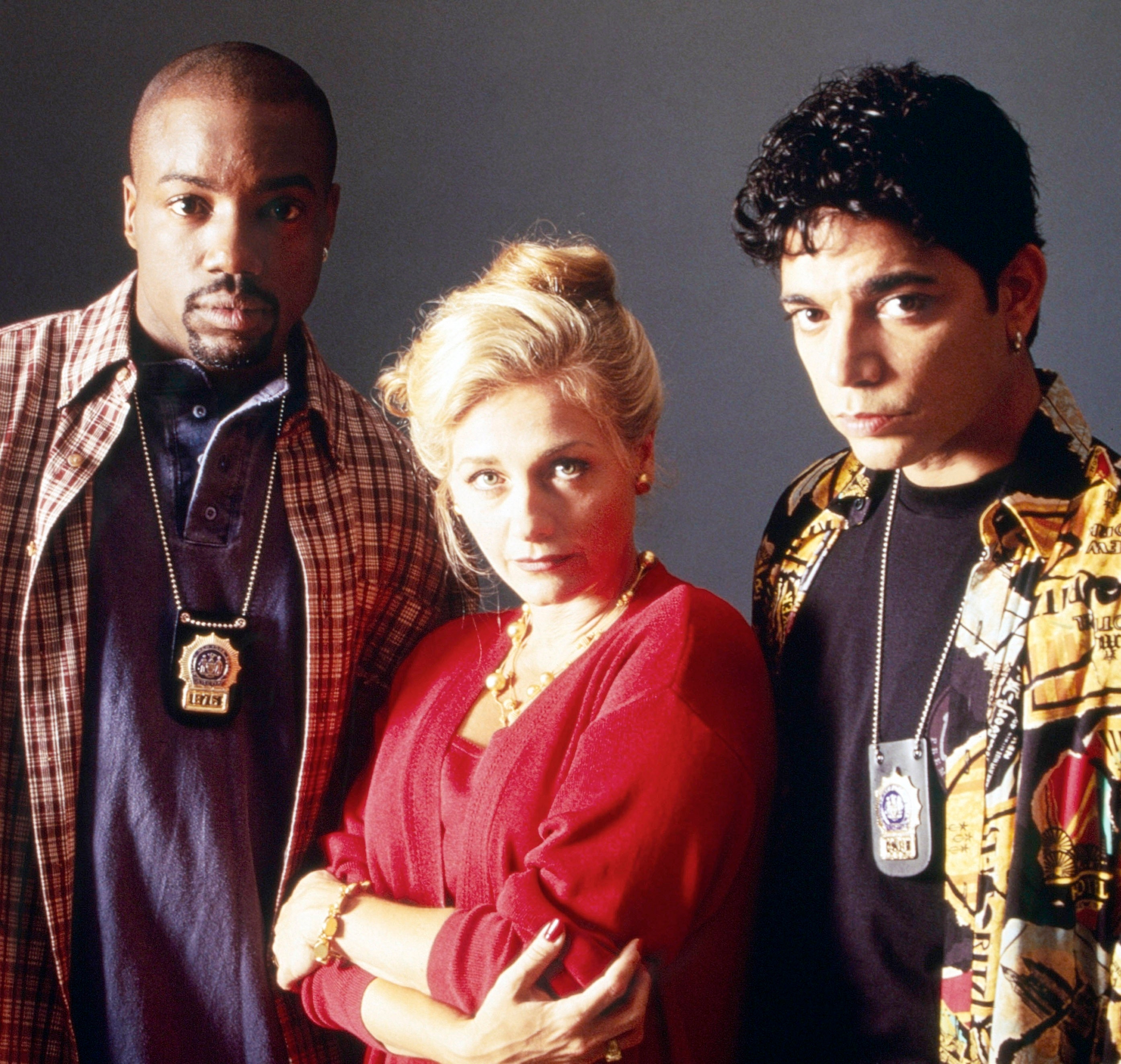 Three actors pose as detectives wearing badges and casual 90s-style clothing in a promotional image for a TV show