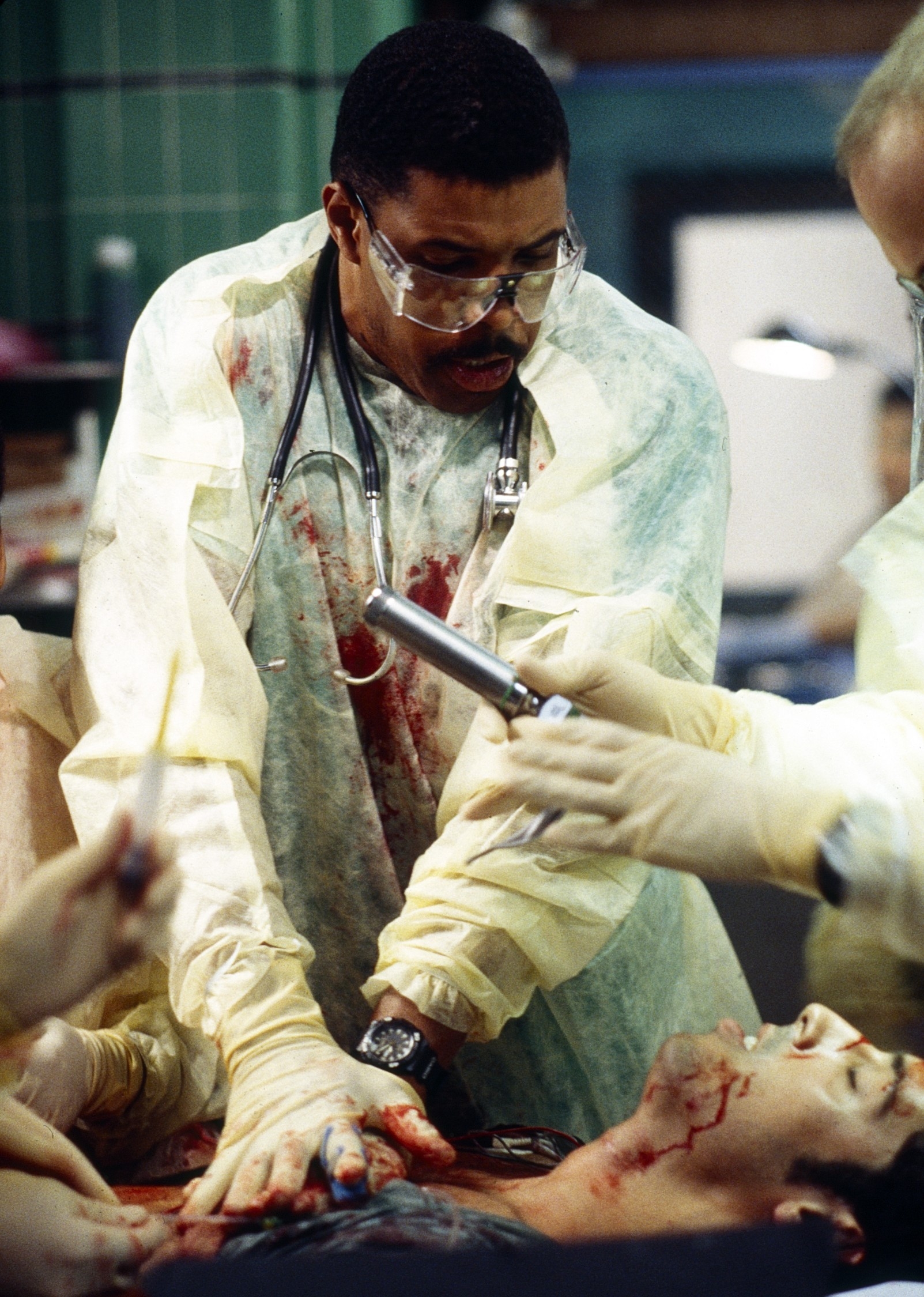 Medical team in a hospital drama scene urgently treating a patient. One doctor wears glasses, a stethoscope, and appears focused and intense