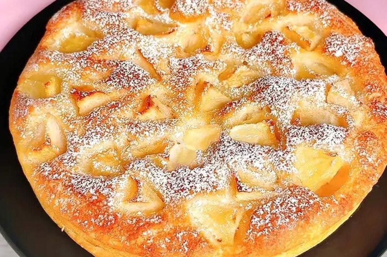 焼きリンゴがトッピングされたパウンドケーキが黒いプレートに載っています。粉砂糖が振りかけられています。