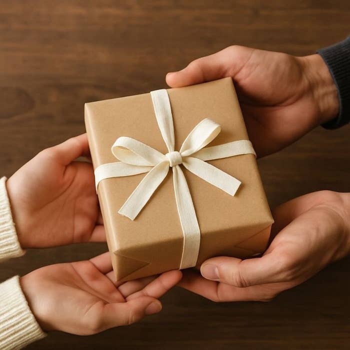 Dos manos entregan un regalo envuelto en papel kraft con un lazo, simbolizando el acto de dar