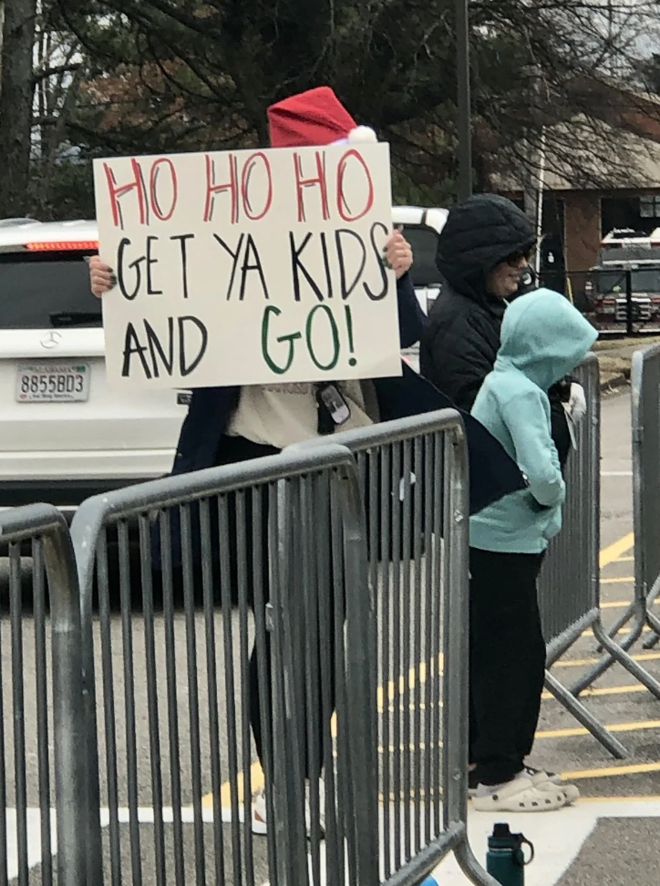 Person holding motion   that reads "Ho Ho Ho, Get Ya Kids and Go!" lasting  down  metallic  barriers adjacent  to 2  others