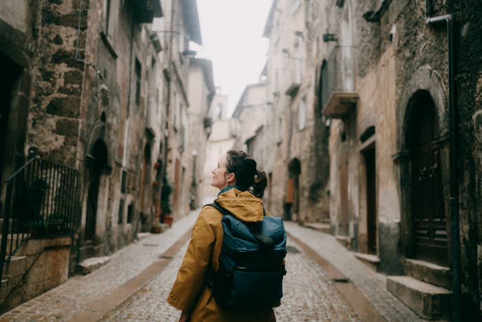 Person with backpack exploring narrow, cobblestone thoroughfare  successful  historic, European village. Perspective shows aged buildings and cozy atmosphere