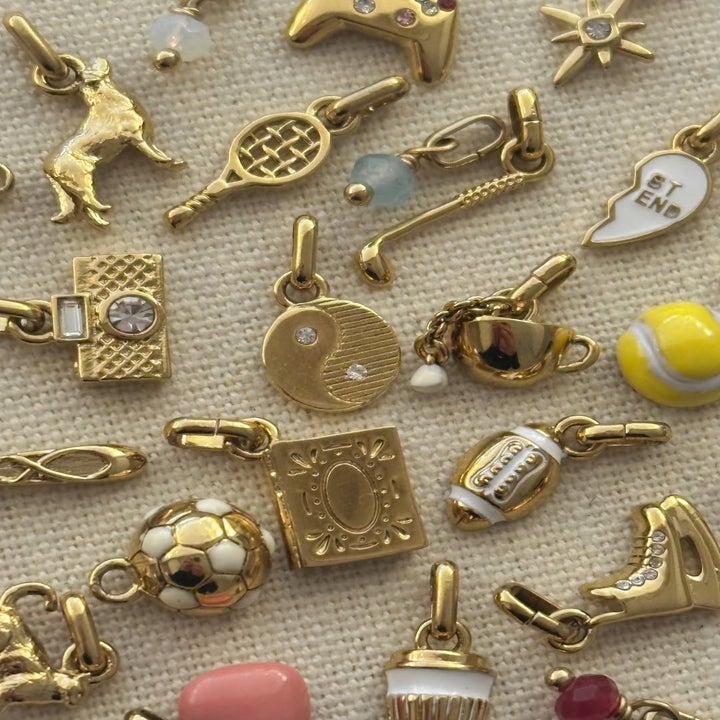 Assorted gold charms on a textured surface, including sports, music, and food-themed designs