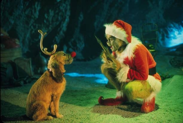 The Grinch, successful  a Santa suit, mischievously talks to his canine  Max, who's wearing antlers and a reddish  nose, successful  a cave-like setting