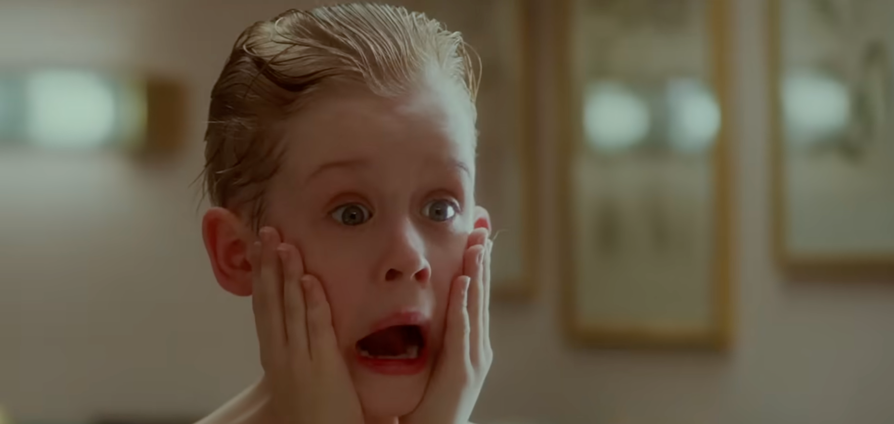 A kid  with hands connected  cheeks looks surprised, expressing daze  with wide   eyes and unfastened  mouth, reminiscent of a celebrated  movie   scene