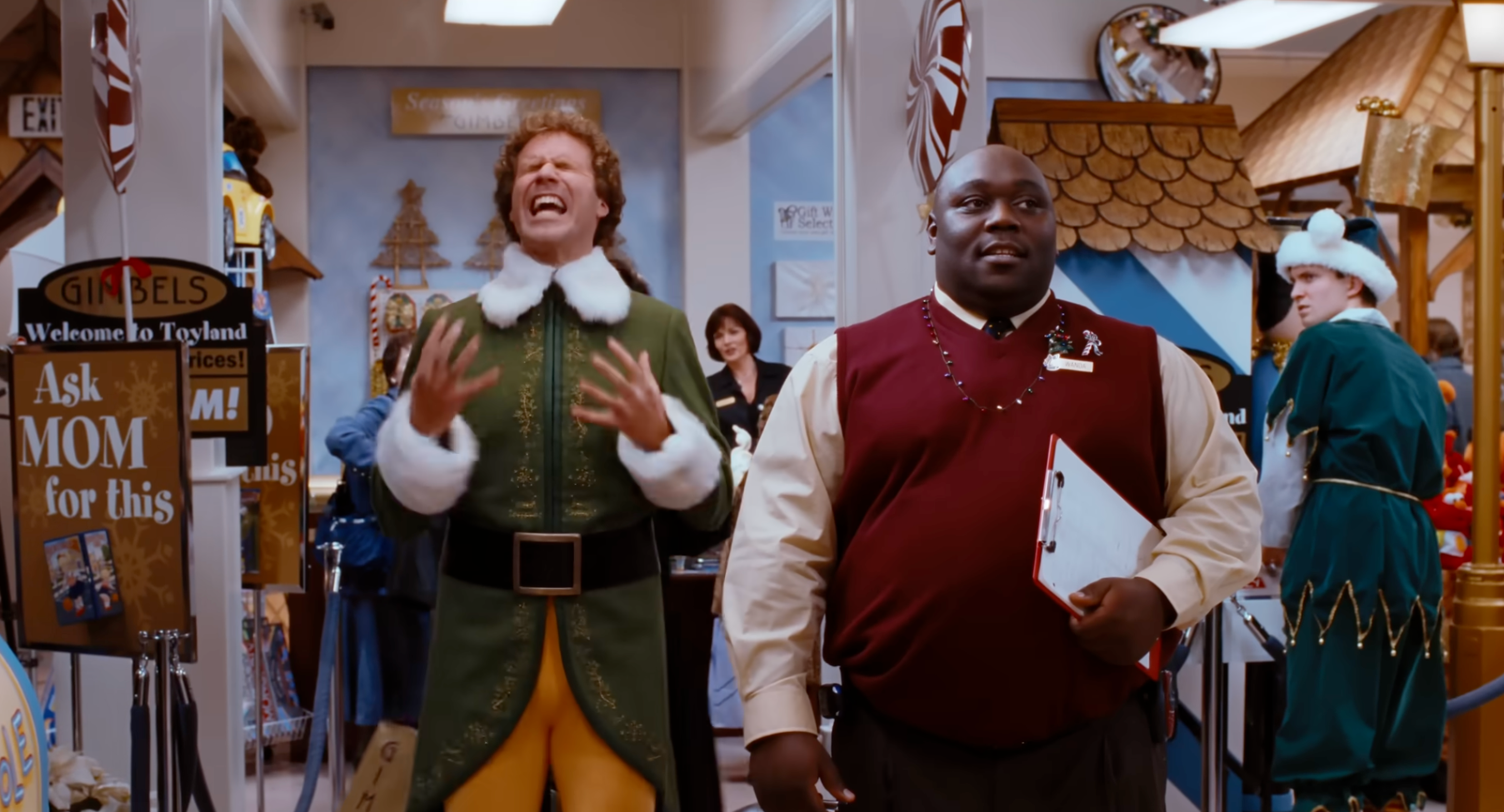 Two actors successful  a engaged  holiday-themed store. One wears an elf costume, gesturing expressively. The different   wears a reddish  sweater vest, holding a clipboard