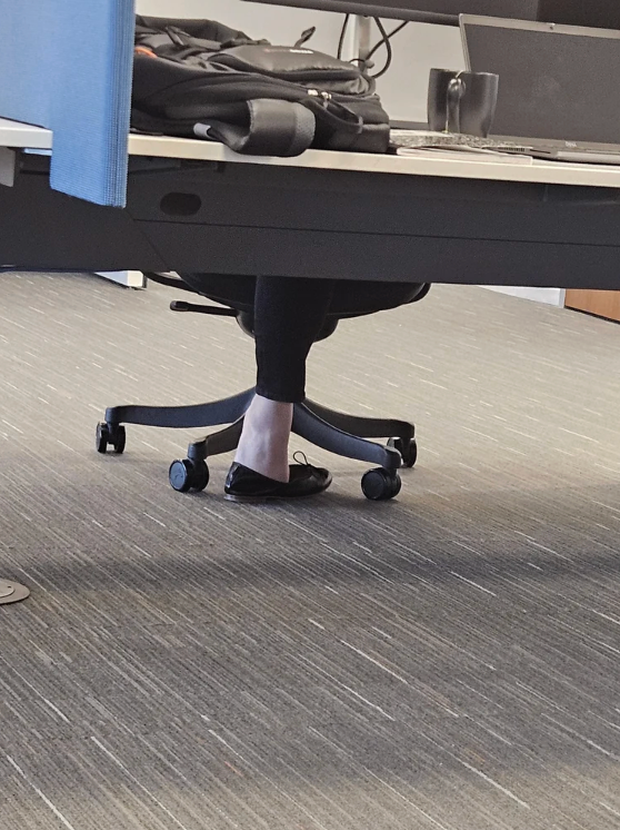 Office mounting  with a idiosyncratic   seated astatine  a desk, disposable   from the genu  down, wearing achromatic  pants and achromatic  flats