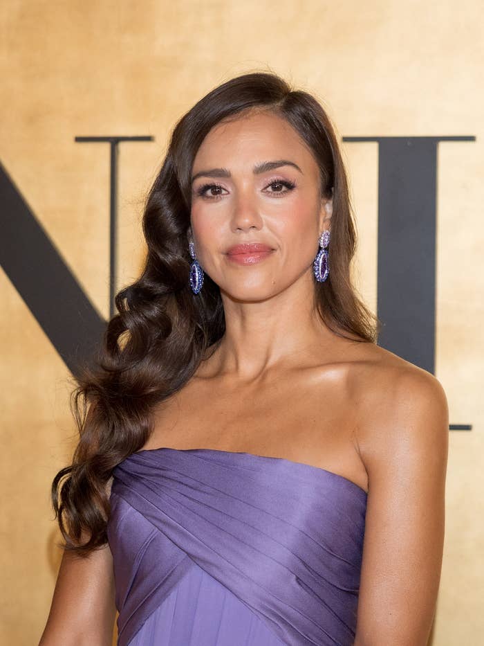 jessica alba in a strapless, elegant gown with side-swept waves and statement earrings poses at an event