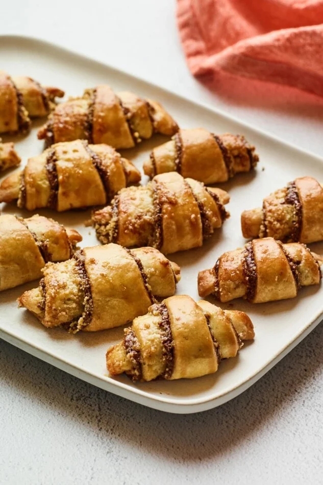 Tray of freshly baked rugelach pastries with visible cinnamon and sugar filling. A cloth napkin is partially visible in the background