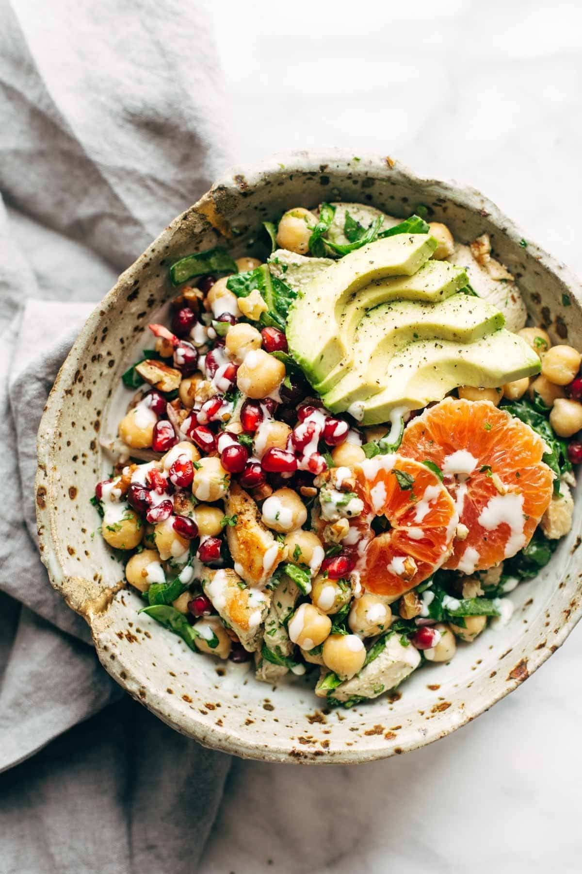 Bowl of chickpea salad with avocado slices, pomegranate seeds, orange slices, and creamy dressing on top
