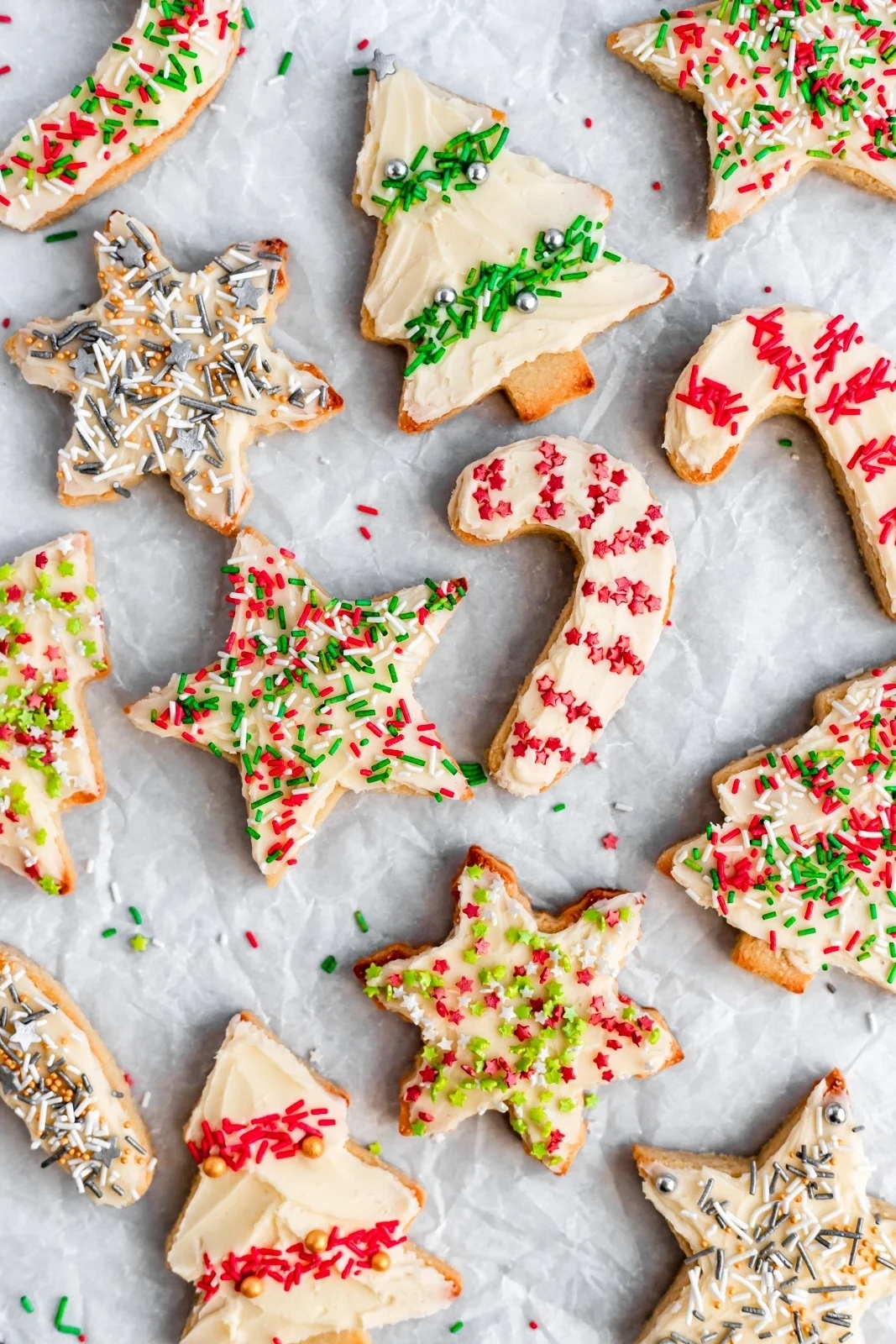 Festive holiday cookies shaped like stars, trees, and candy canes, decorated with sprinkles and icing, arranged on parchment paper