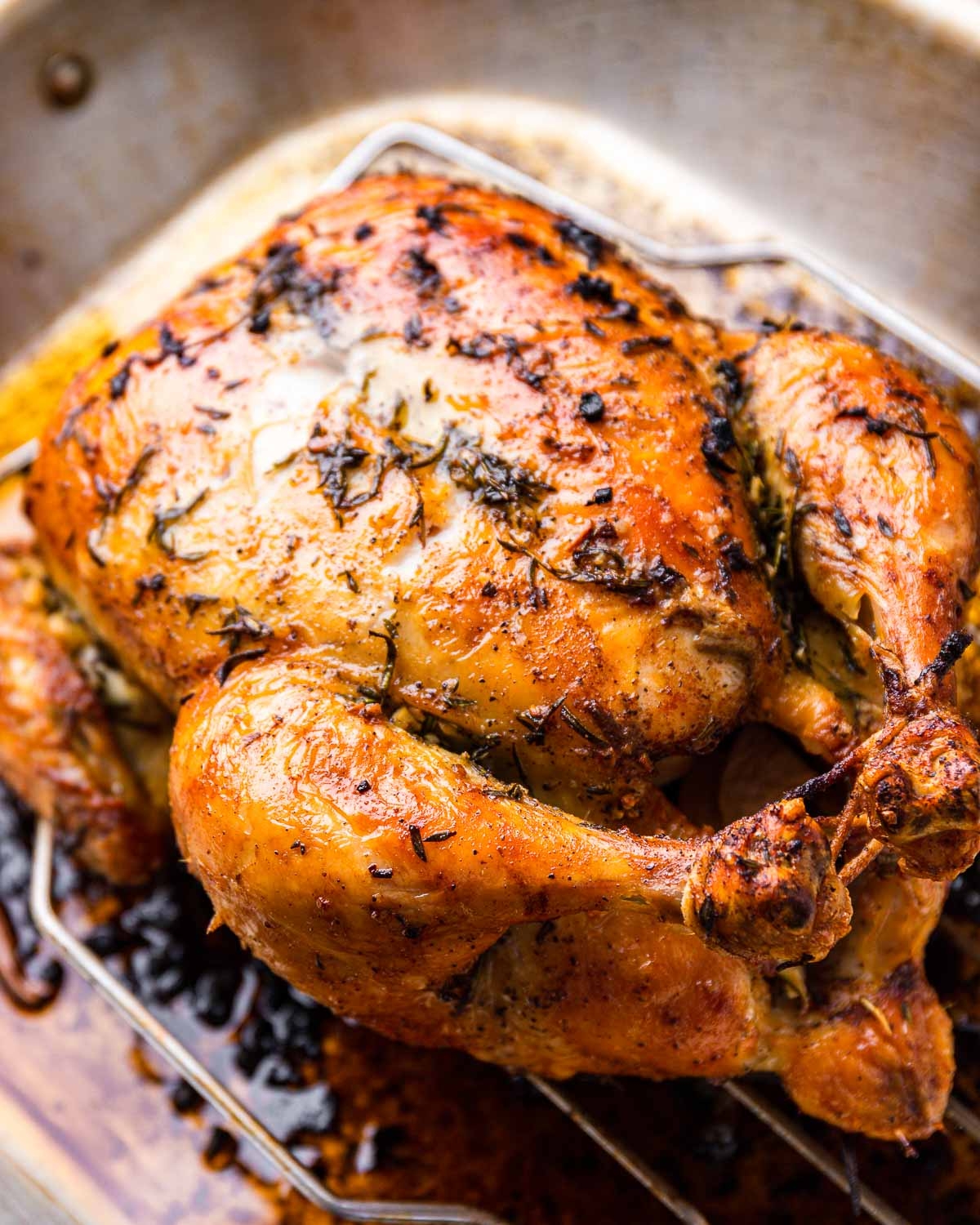 Roasted chicken seasoned with herbs on a rack in a baking pan