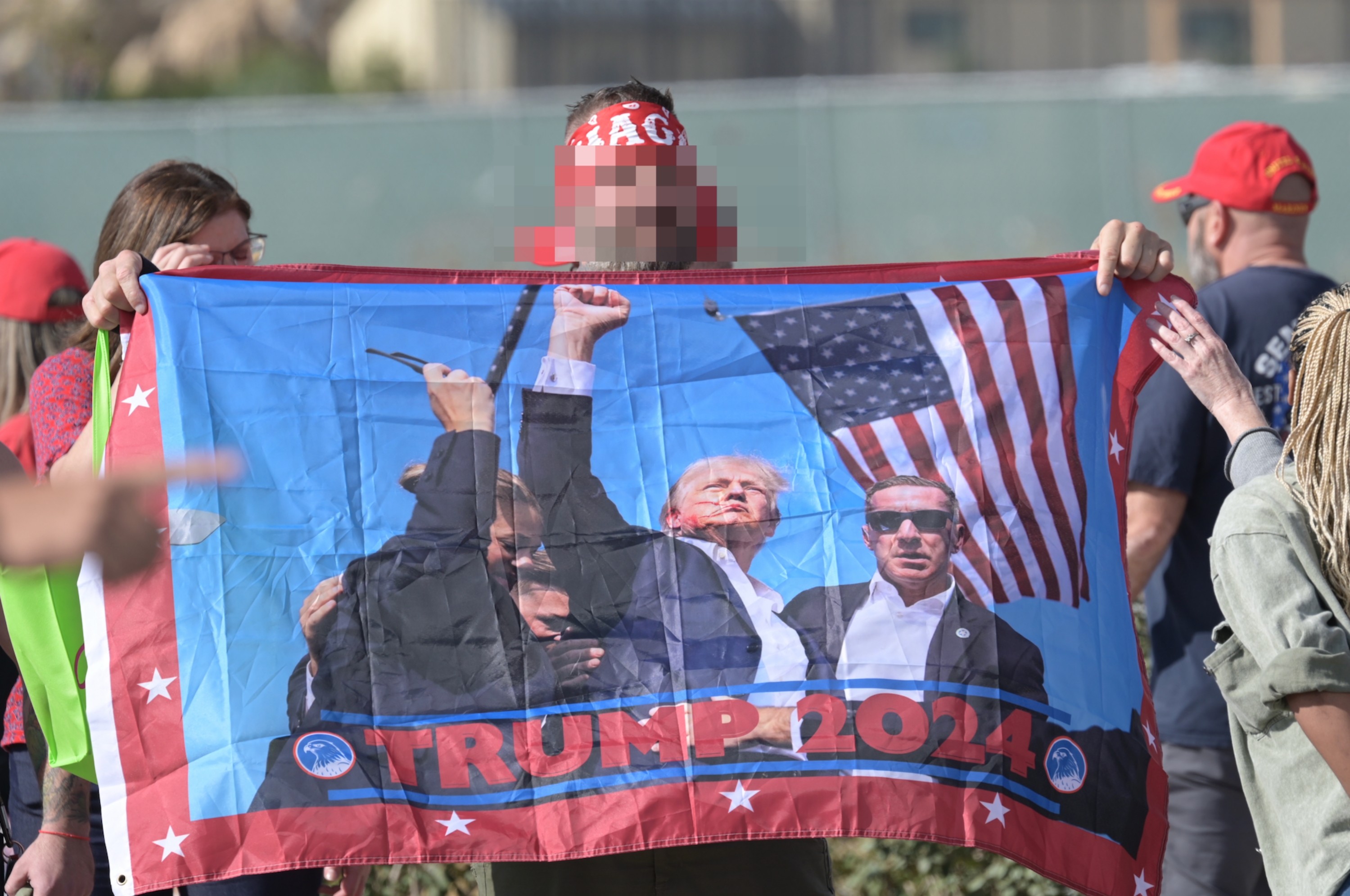 Person holding a &quot;Trump 2024&quot; flag with images of Donald Trump and supporters waving an American flag