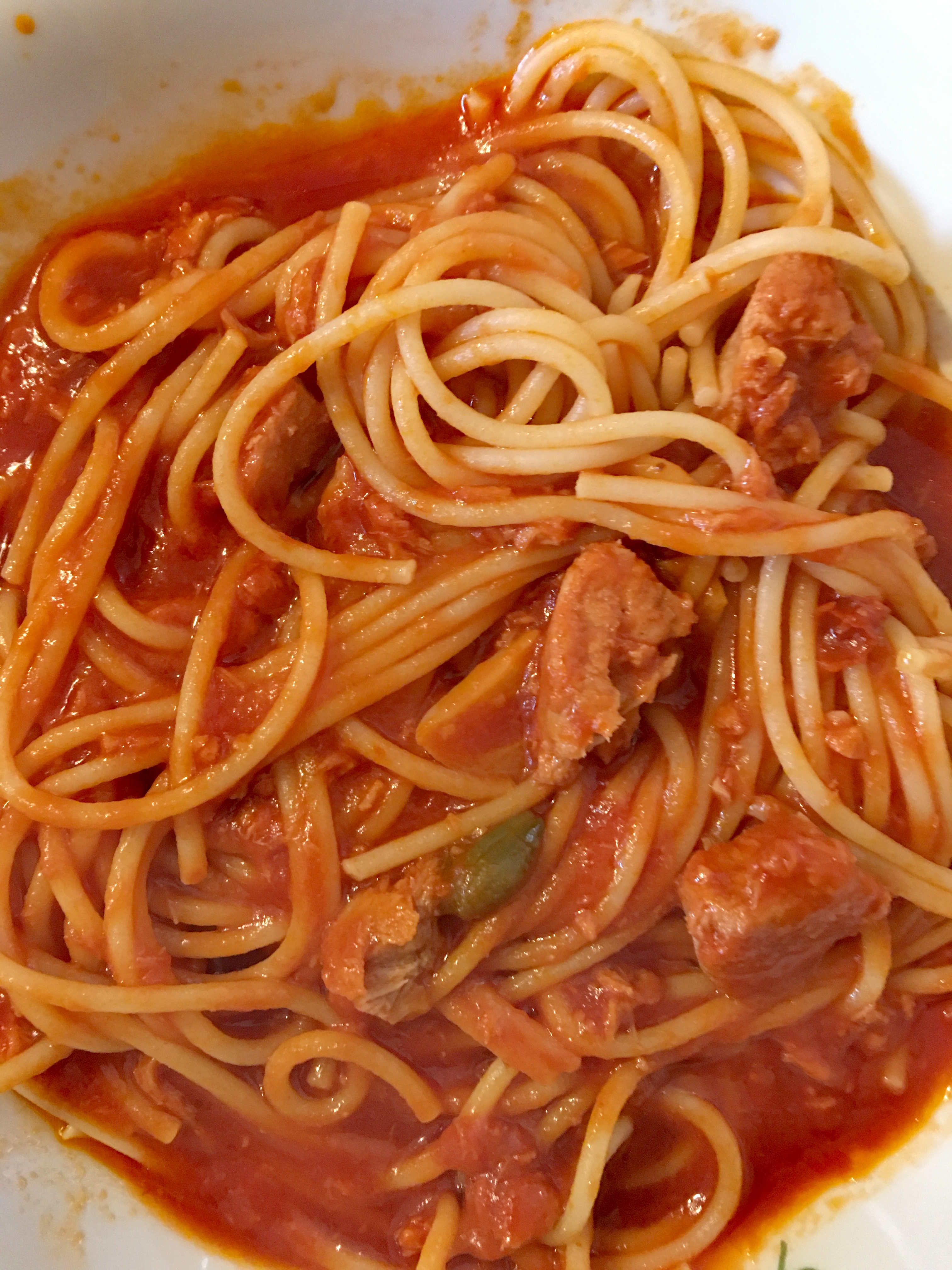 Spaghetti with sausage pieces in a tomato-based sauce on a white plate