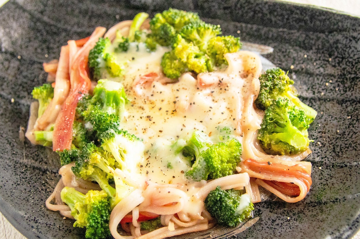 ブロッコリー、カニ風味かまぼこ、チーズがのったパスタ料理が黒い皿に盛られている。