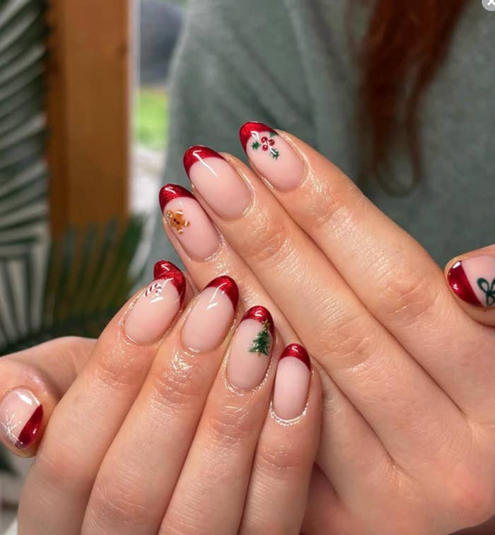 Manos con uñas decoradas con diseños navideños, incluyendo flores y un árbol de Navidad en cada uña