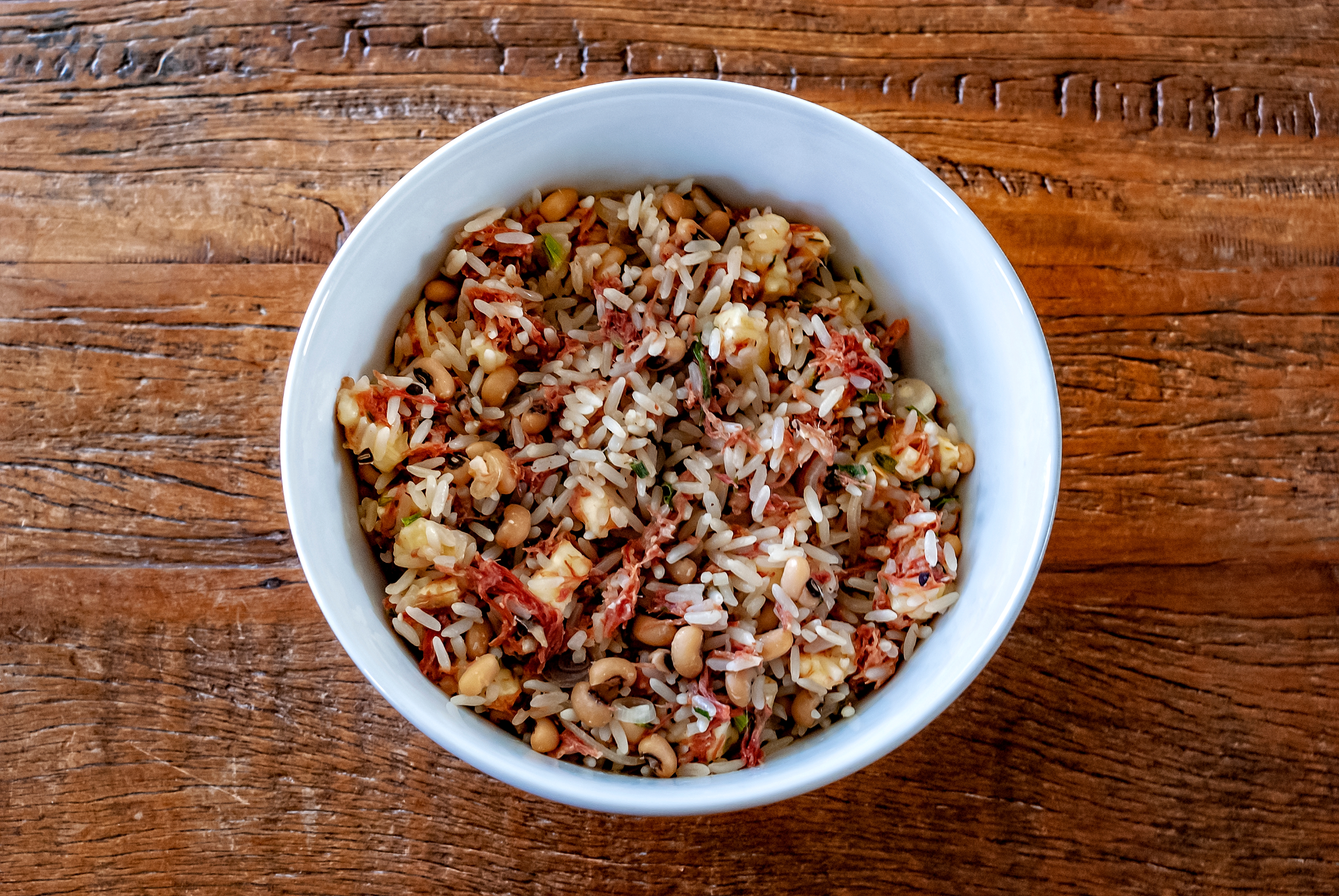 A bowl of rice salad mixed with beans, diced vegetables, and herbs on a wooden table