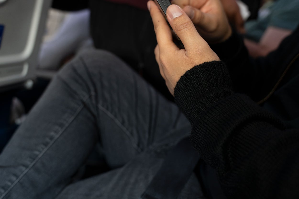 飛行機の座席で携帯電話を操作している人。周囲に他の乗客も見える。