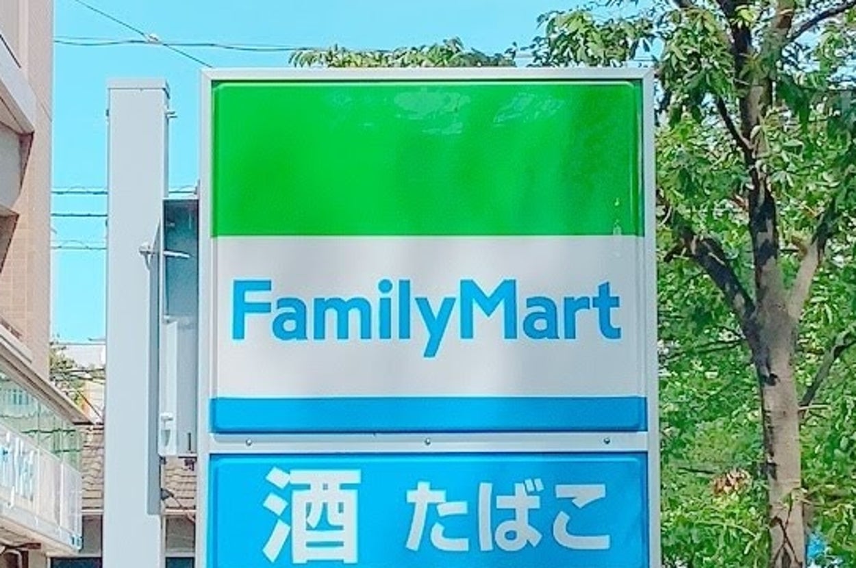 ファミリーマートの看板。酒、たばこの文字が書かれている。周りに緑の木と建物が見える。