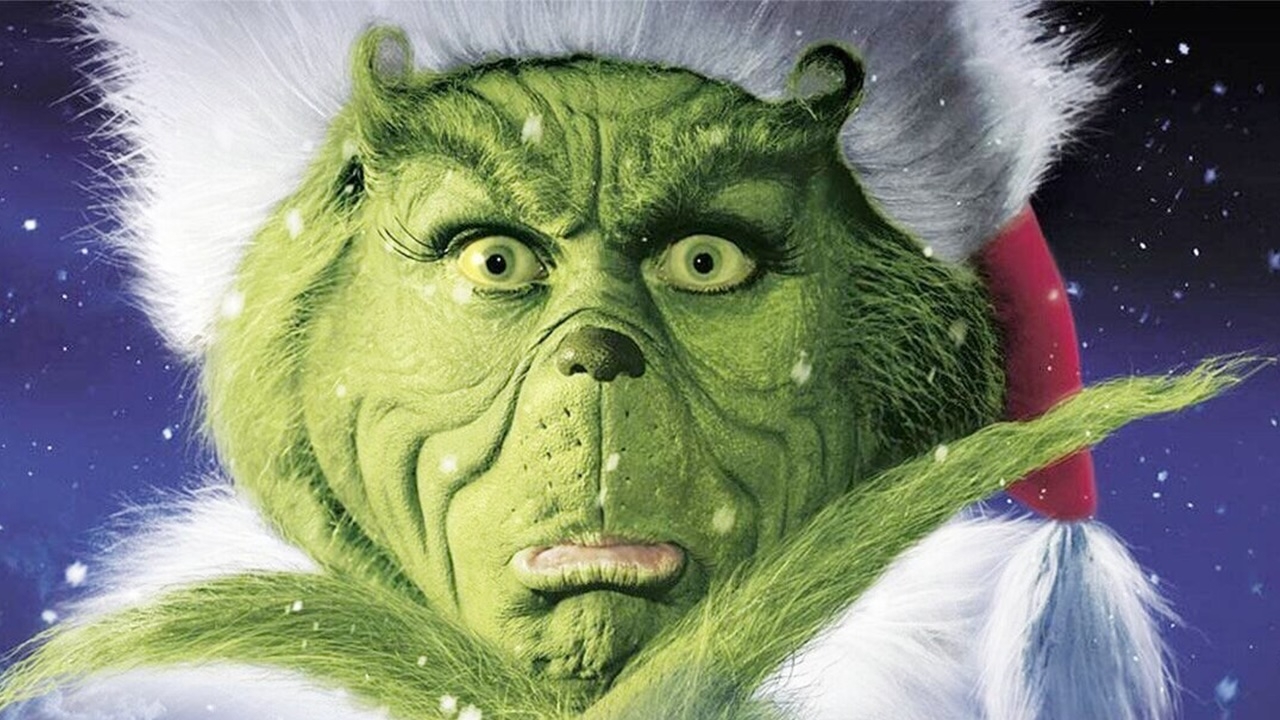 The Grinch grumpily poses successful a Santa chapeau and fluffy collar, showcasing his iconic scowl against a snowy backdrop