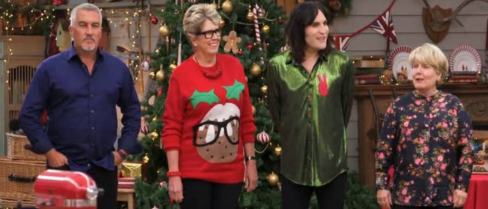Four people stand in front of a decorated Christmas tree. One wears a festive sweater, another sports a shiny green shirt, and two others wear patterned tops