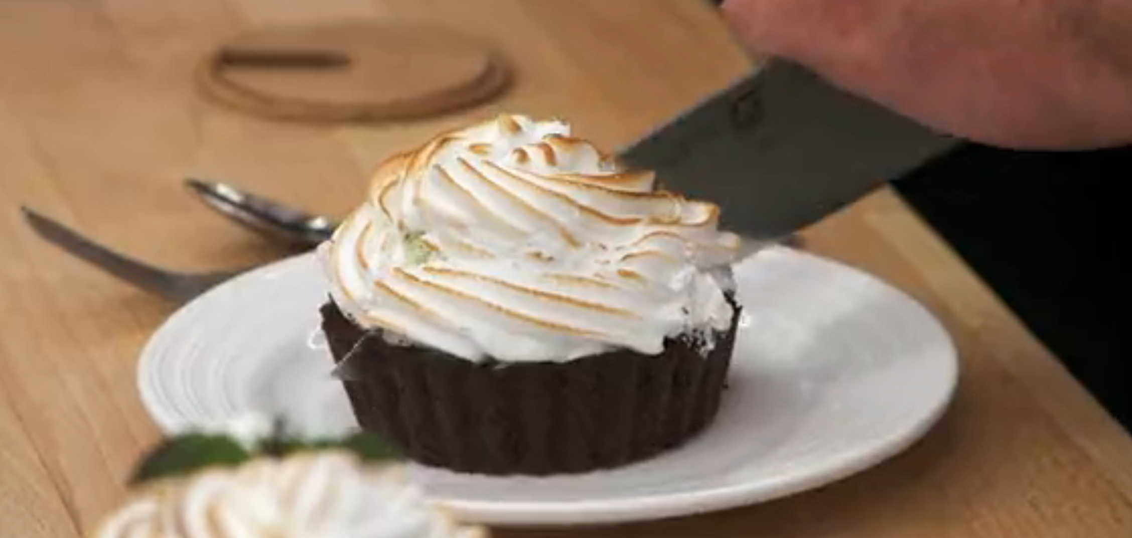 A chocolate tart with a swirled meringue topping is being sliced on a white plate