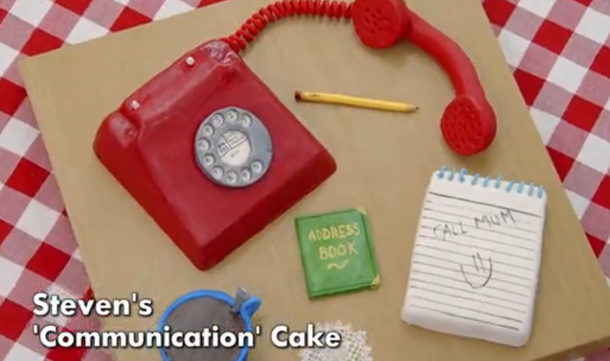 Cake shaped like a red rotary phone with a notepad, pencil, and green address book. The notepad reads "Call Mum" with a smiley face