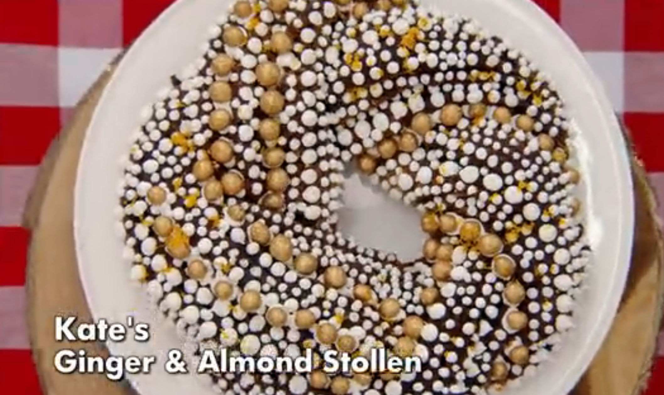 Ginger and almond stollen topped with powdered sugar and gold decorations on a white plate, text reads "Kate's Ginger &amp;amp; Almond Stollen."