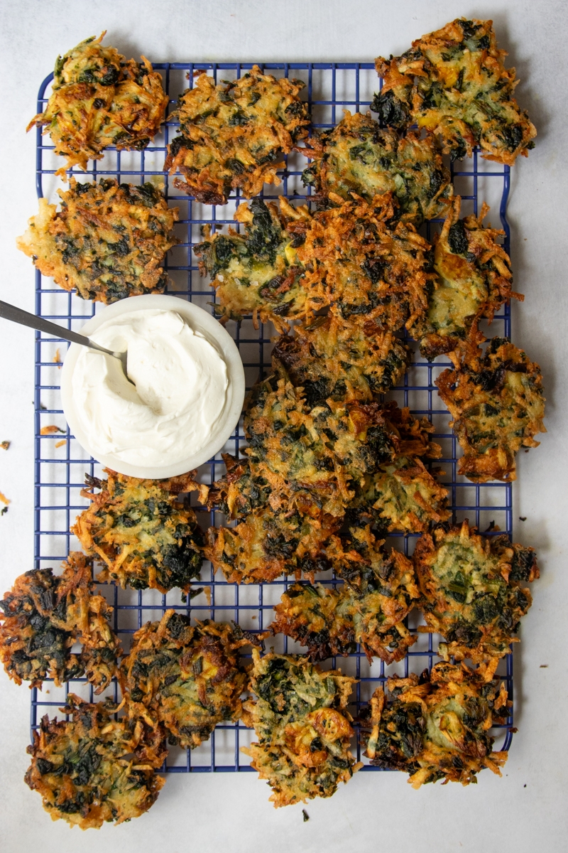 Crispy vegetable fritters on a cooling rack with a bowl of creamy dip and a spoon beside them