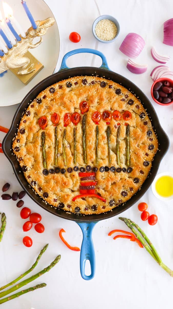 Rosh Hashanah skillet bread decorated with asparagus, cherry tomatoes, and black olives to resemble a menorah, surrounded by various vegetables