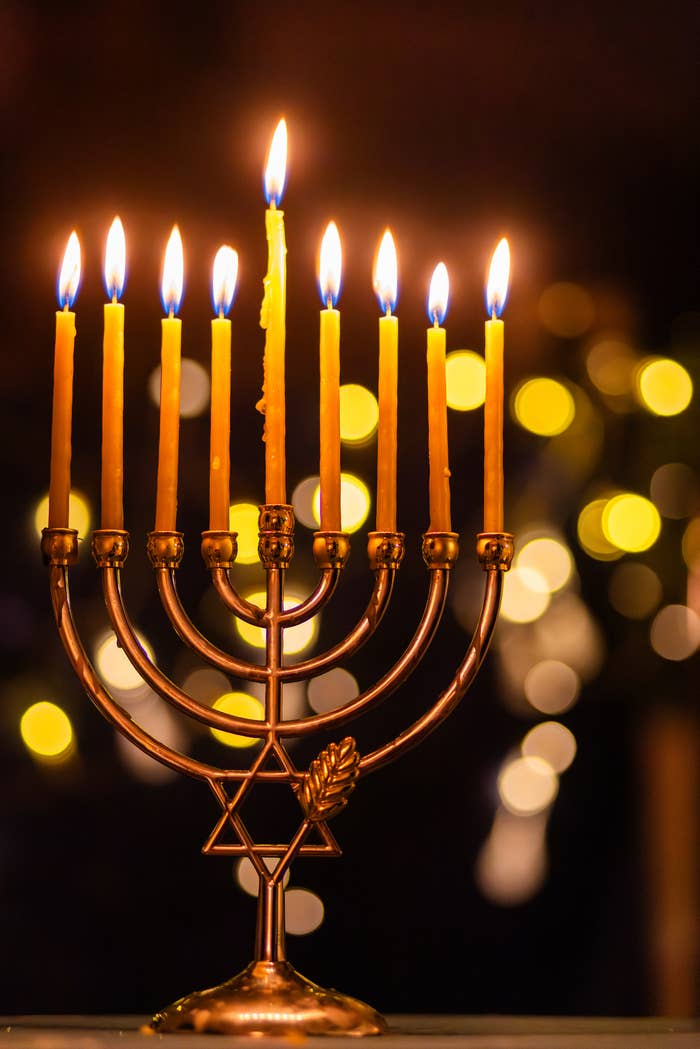 Lit menorah with all nine candles burning, set against a blurred background of warm lights, signifying Hanukkah celebration