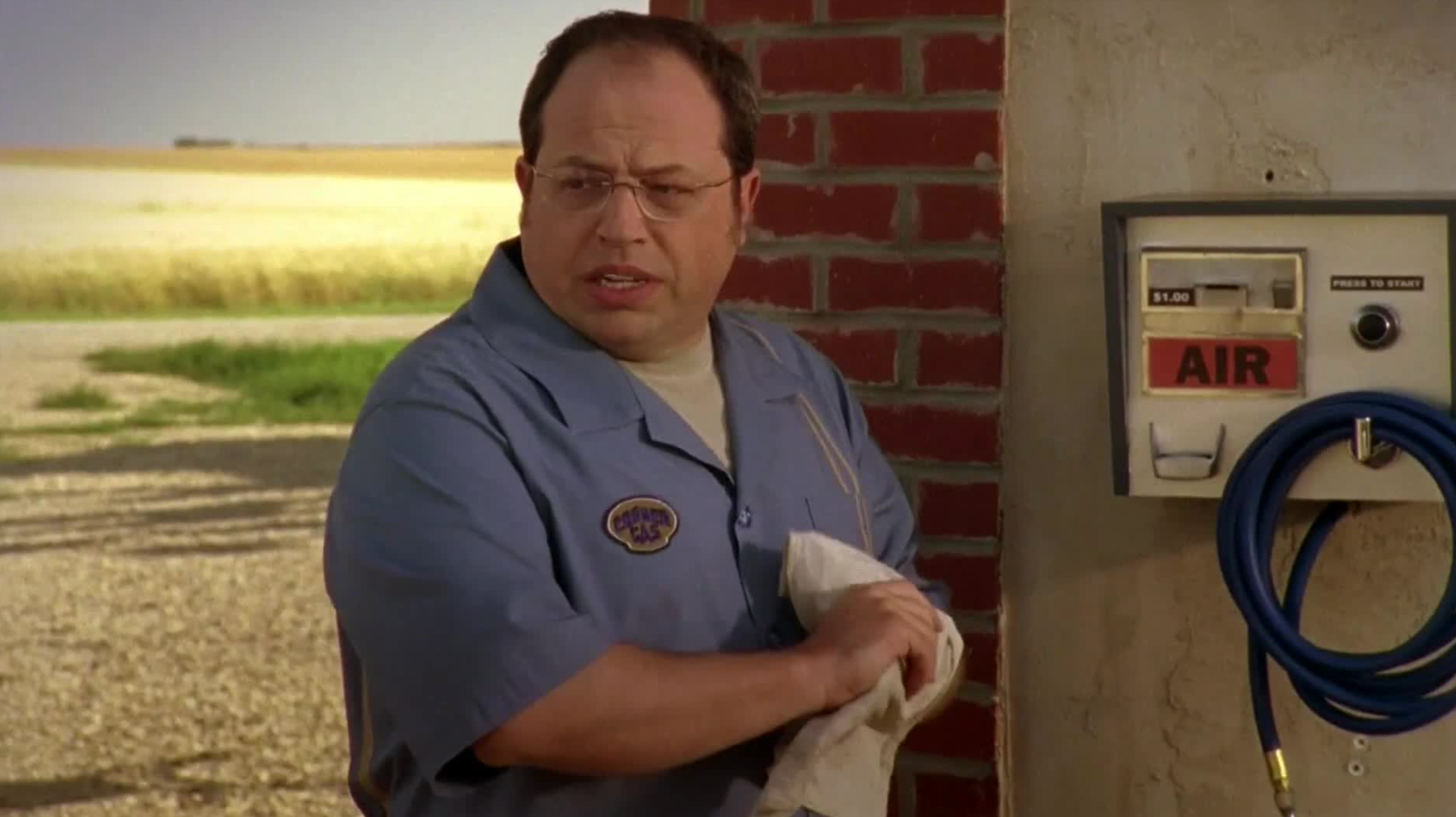 Mann i arbeidsuniform som holder en klut, står ved siden av en luftpumpe, utendørs. Ser forvirret eller bekymret ut