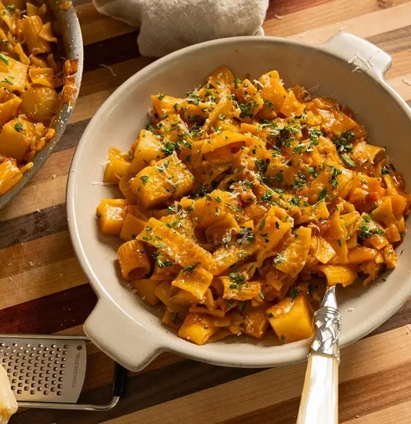 Pasta dish served in a bowl with chopped herbs on top, next to a napkin and a grater on a wooden board