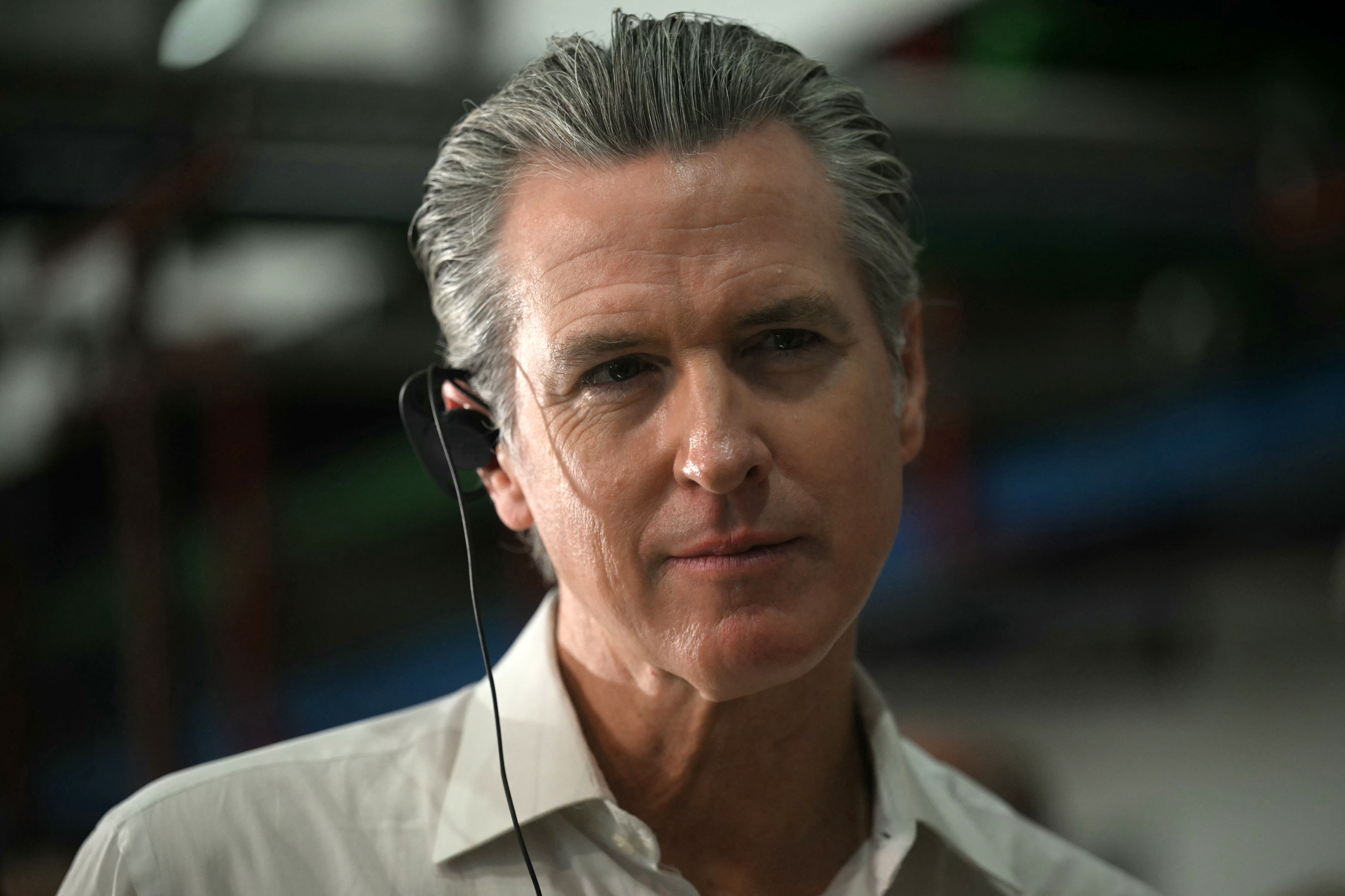 En person med hodesett ser oppmerksomt fremover, kledd i en formell hvit skjorte, og antyder engasjement i en begivenhet eller diskusjon