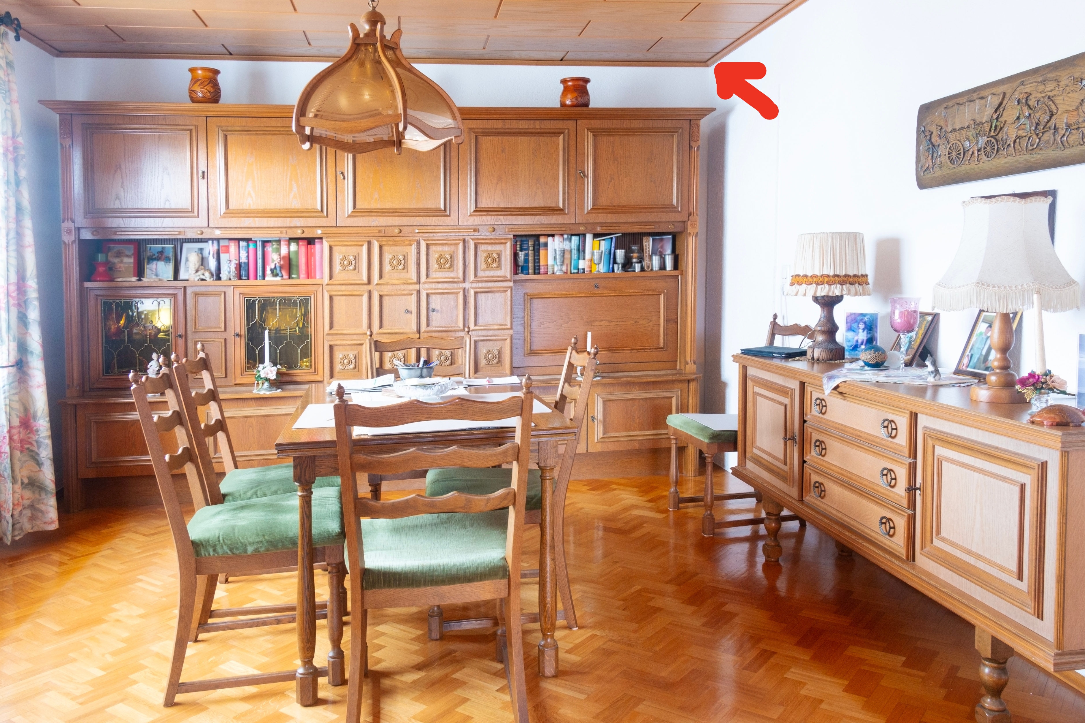 Dining country   with woody  furniture, including a array  with chairs and a cabinet. Books are connected  a shelf, with lamps and decor connected  sideboard. Bright, cozy setting