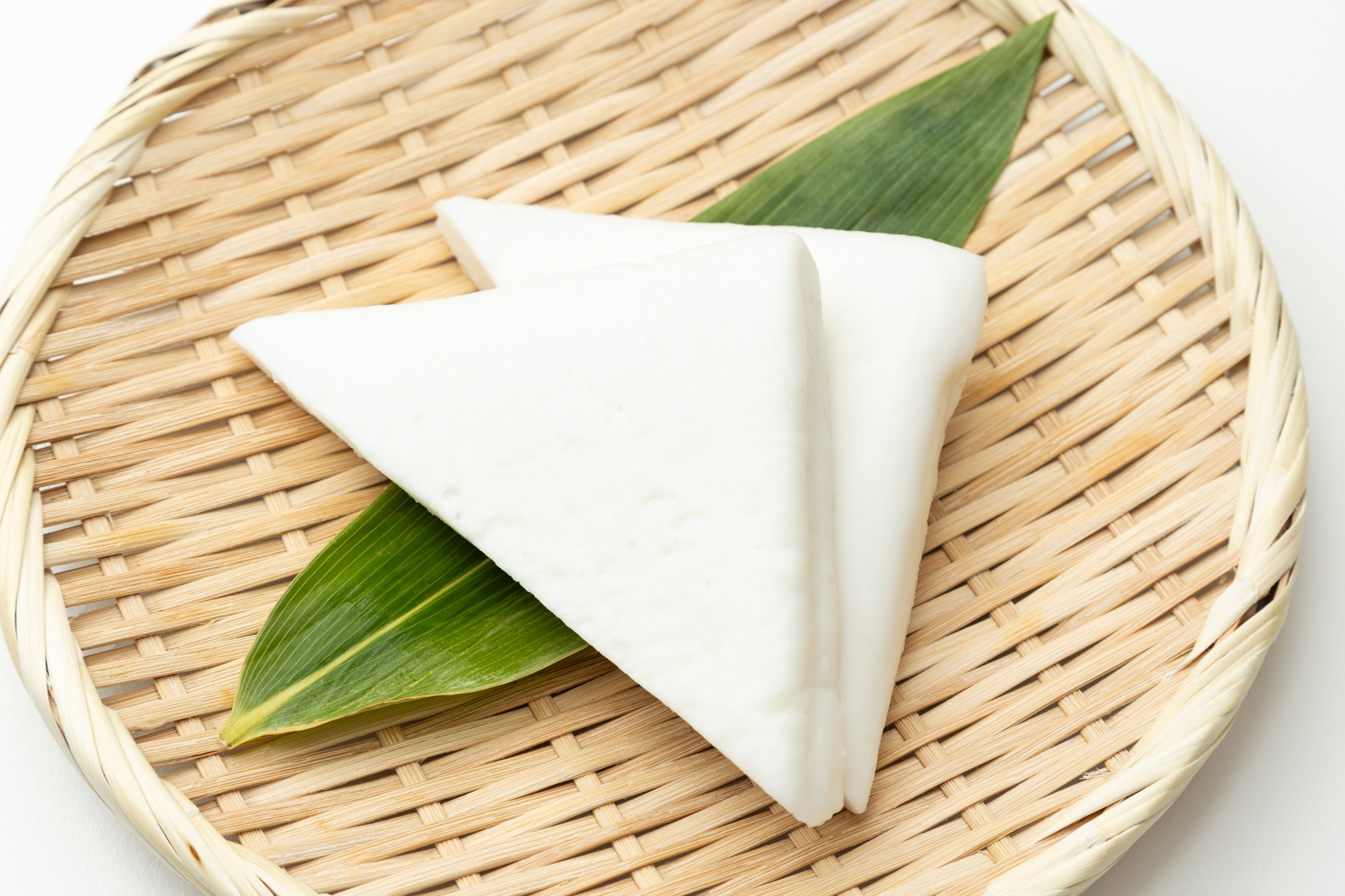 竹の葉の上に置かれた三角形の白いかまぼこが、竹製のざるにのっています。