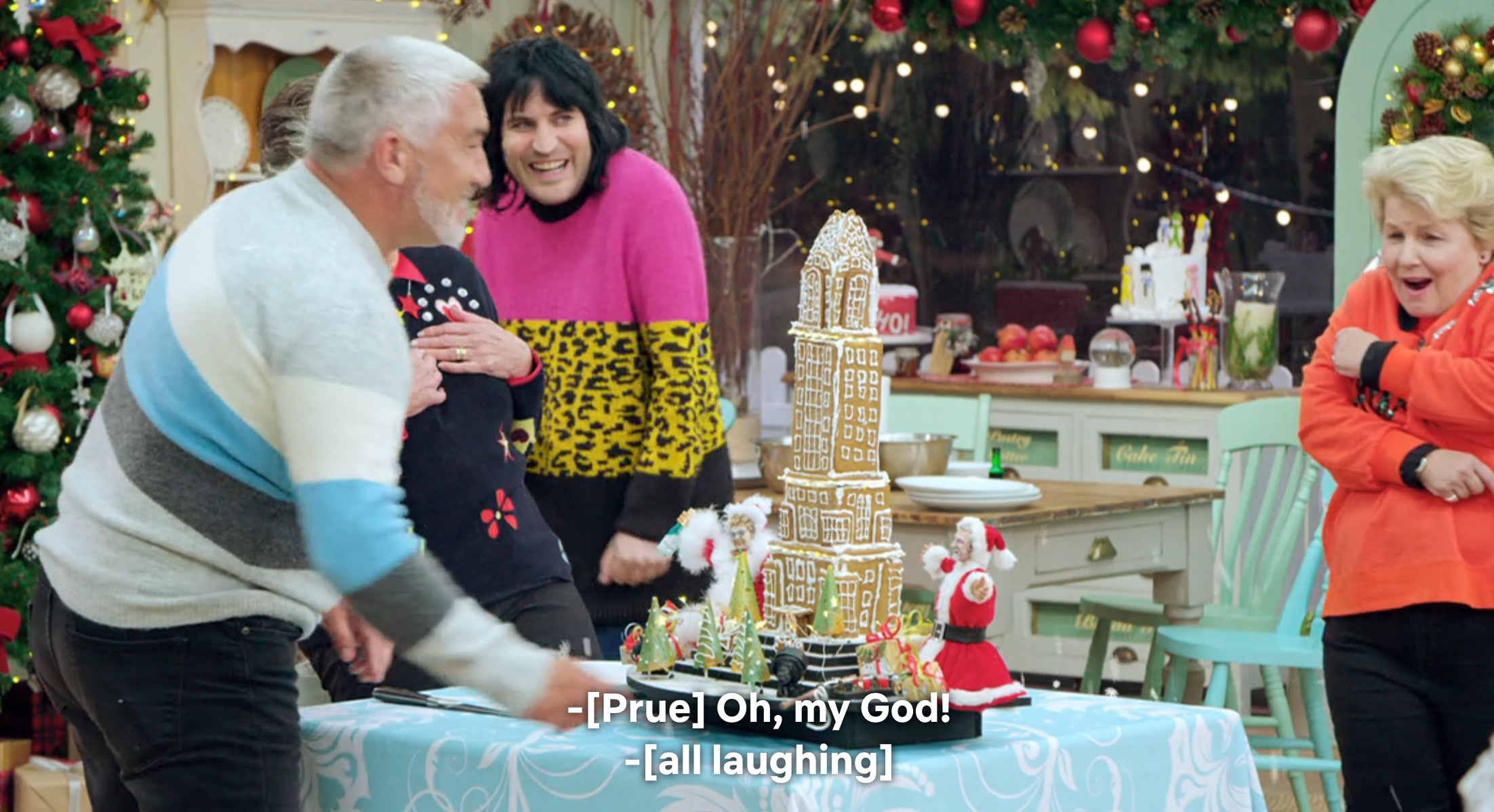 People laughing near a gingerbread replica of Big Ben on a festive set with holiday decor