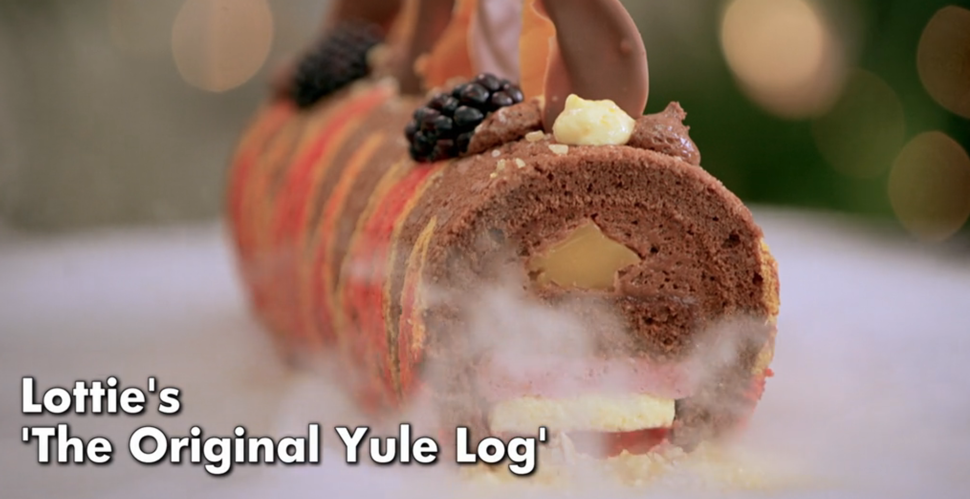 Festive Yule log cake garnished with blackberries and cream, featuring a text overlay: "Lottie's 'The Original Yule Log'."