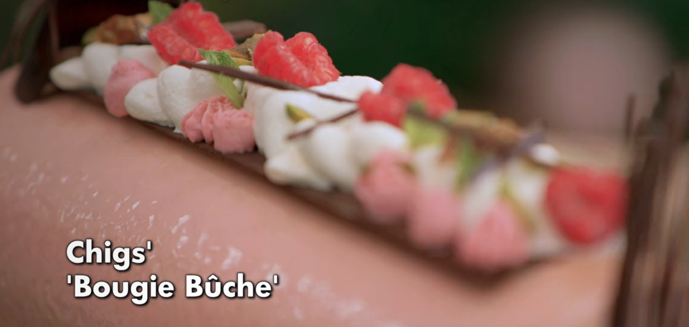 Close-up of a decorative pastry labeled "Chigs' 'Bougie Bûche'" with whipped cream, raspberries, and chocolate details
