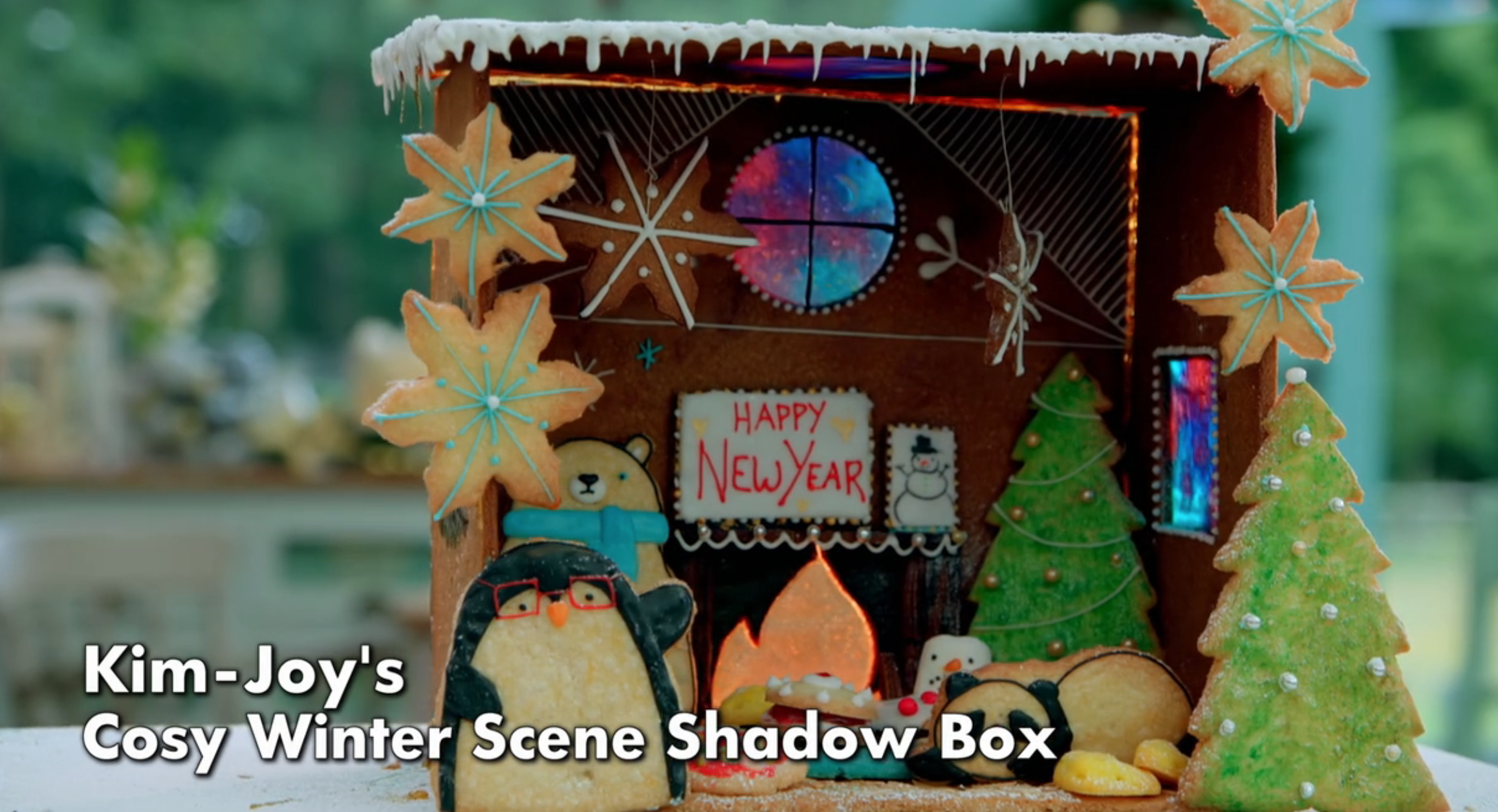 Gingerbread shadow box by Kim-Joy featuring penguins, a New Year sign, a Christmas tree, and cookies in a cozy winter scene