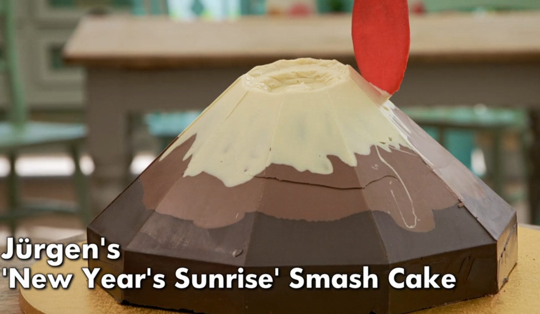 A geometric smash cake shaped like a mountain with layered chocolate and a red decoration, labeled "Jürgen's 'New Year's Sunrise' Smash Cake."