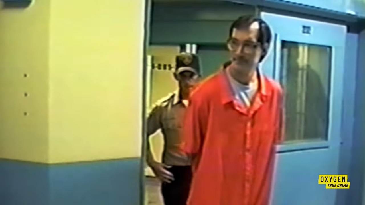 En mann i en oransje fengselsdress blir ledet av en vakt i en gang. Innstillingen ser ut til å være en kriminalomsorg