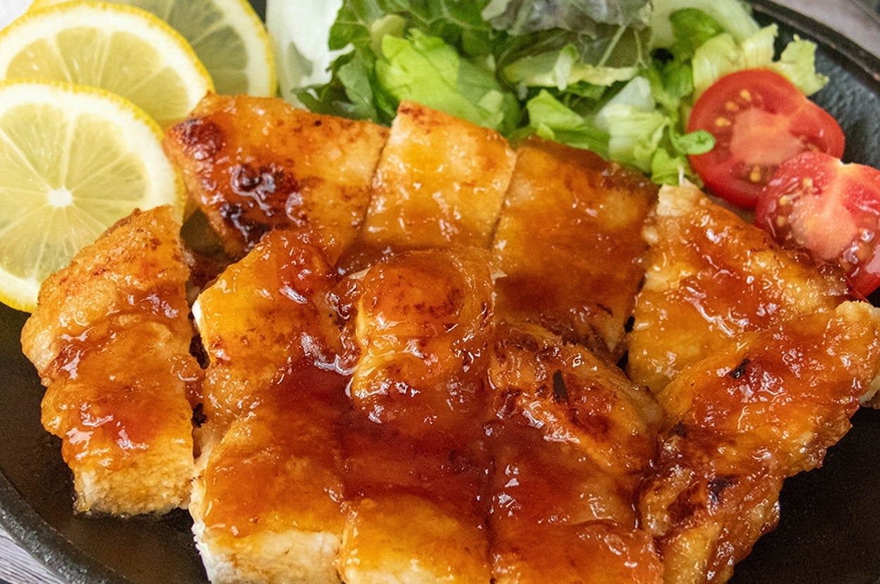 レモンスライスとサラダを添えた鶏むね肉のはちみつレモンチキンが黒いプレートに盛られている。