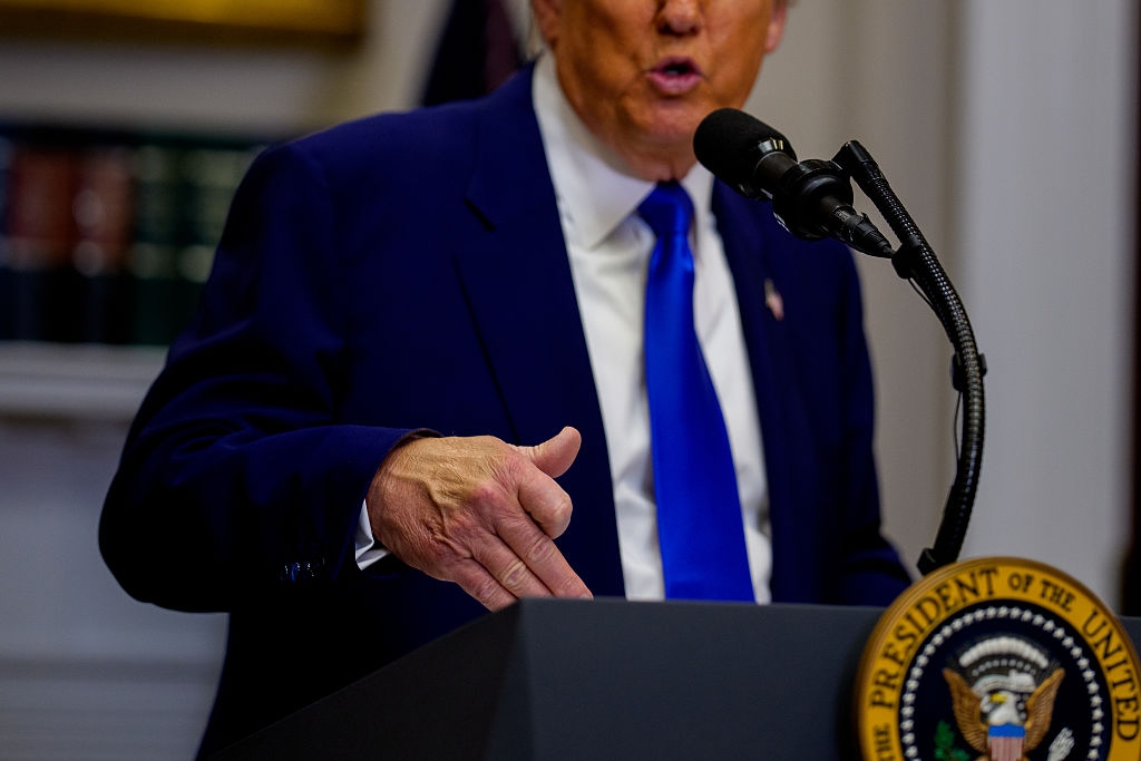 Person som snakker på et podium med en presidentsegl, gestikulerer med en hånd, kledd i dress og slips